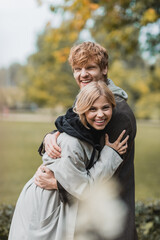 Fototapeta premium cheerful young man and woman in autumnal coats embracing each other and smiling in park.
