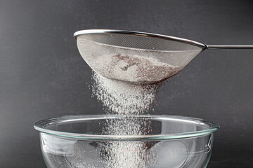 Sieve and powdered sugar on black background