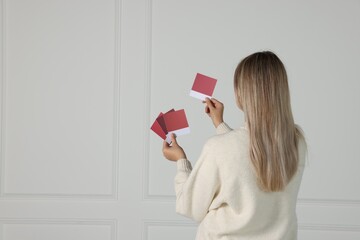 Woman with color sample cards choosing paint shade for wall indoors, back view. Interior design