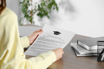 Student with acceptance letter from university at wooden table indoors, closeup