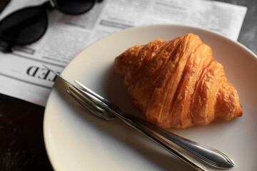 Tasty croissant, newspaper and sunglasses on black table, closeup