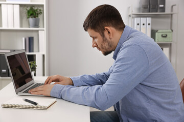 Naklejka na ściany i meble Man with poor posture working on laptop in office. Symptom of scoliosis