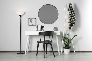 Stylish room interior with round mirror on white wall over desk