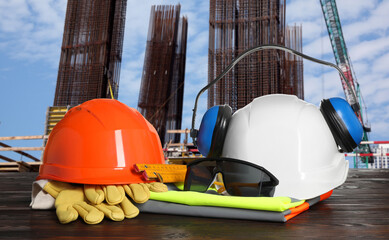 Safety equipment and tools on wooden surface and blurred view of construction site
