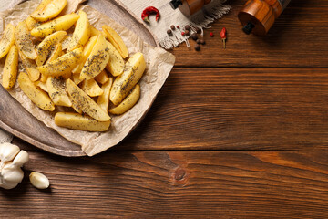 Board with tasty baked potato wedges and spices on wooden table, flat lay. Space for text
