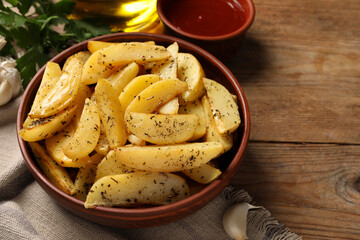 Bowl with tasty baked potato wedges, sauce and spices on wooden table