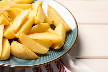 Plate with tasty baked potato wedges on white wooden table, closeup