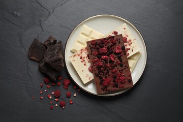Chocolate bars with freeze dried fruits on black table, flat lay