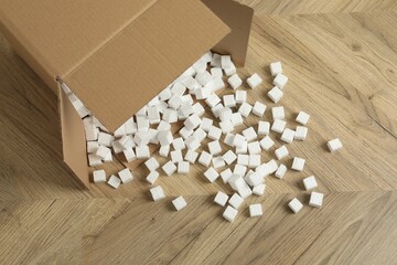 Overturned cardboard box with styrofoam cubes on wooden floor, above view