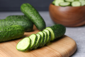 Whole and cut fresh ripe cucumbers on wooden board, closeup