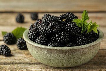 Bowl with fresh ripe blackberries on wooden table, closeup