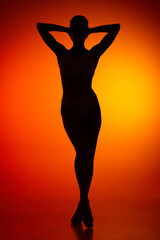 Silhouette of female full-length body isolated over orange background. Relaxation, wellness