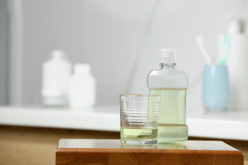 Bottle and glass with mouthwash on wooden table in bathroom, space for text