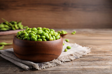 Bowl of delicious edamame beans on wooden table, space for text