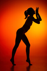Fototapeta na wymiar Silhouette of female full-length body isolated over orange background. tender movements