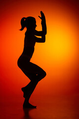 Fototapeta na wymiar Silhouette of female full-length body isolated over orange background. Well coordinated movements