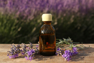 Bottle of natural lavender essential oil and flowers on wooden table outdoors