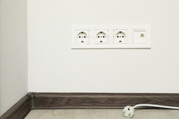 Plug near white wall with power sockets indoors. Electrical supply