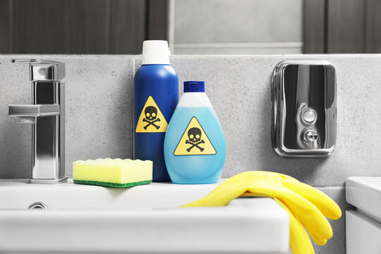 Bottles of toxic household chemicals with warning signs, gloves and scouring sponge in bathroom