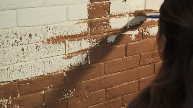 girl paints a brick white wall in brown, coffee color , brush stirs paint