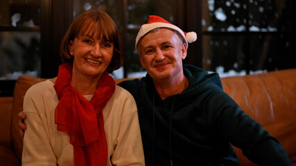Portrait of happy smiling senior couple wearing santa hats celebrating at home on Christmas Eve