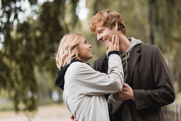 redhead man and blonde woman in coat smiling while having date in park.