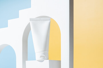 Cream tube with cream branding concept on cocncrete podium on blue and yellow background. Cosmetic skincare product blank plastic package. White unbranded lotion, balsam, hand creme, toothpaste mockup