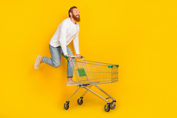 Full size profile photo of beard man run trolley wear shirt jeans shoes isolated on yellow color background