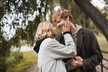 cheerful redhead man and blonde woman in coat smiling during date in park.