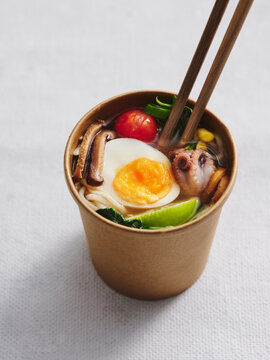 Vertical shot of seafood ramen in take away cup on white background