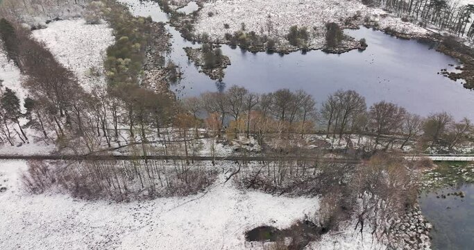Aerial view, flying sidewards and looking down, of walking path and lakes in nature area Witte Veen covered with snow, Overijssel, Netherlands