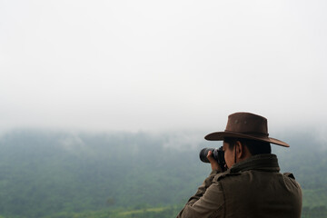 Fototapeta na wymiar Professional photographer in hat takes photos with digital camera on the mountains with clouds and fog