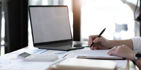 Young business woman sitting at table and taking notes in notebook.On table is laptop, smartphone