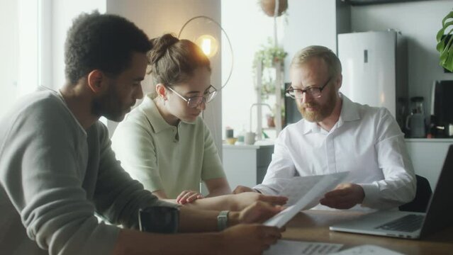 Financial advisor explaining documents to young couple while giving at home consultation about investment plan development