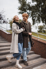 joyful woman and happy redhead man with umbrella descending stairs in park.