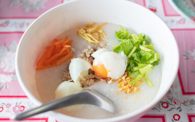Porridge in a white bowl with seasonings and meat, carrots, ginger, garlic, boiled egg.