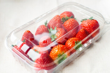 Sweet fresh strawberries in plastic container on the table. Supermarket shop plastic box container with red fruits.