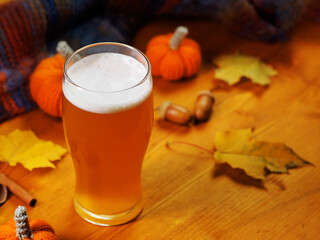 Pumpkin ale in a glass on a wooden table. Autumn decor with maple leaves, scarf, acorns and cinnamon