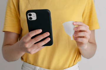 young woman with menstrual cup and phone reads instructions close-up. hypoallergenic silicone cup...