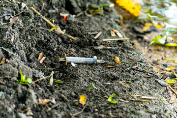 Used dirty syringe left after injection of the drug lying on the ground by the river bank. Intravenous drug use, the spread of AIDS and HIV, through drug addiction.