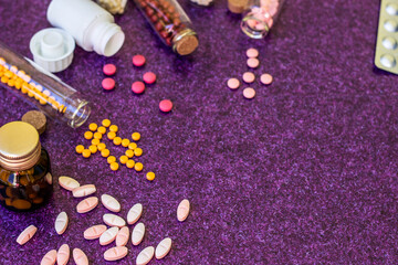 Medical bottles and medication pills spilling out on to purple background