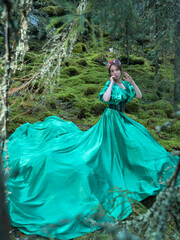 A beautiful woman in a long green dress with a corset and a decorative crown of branches and...