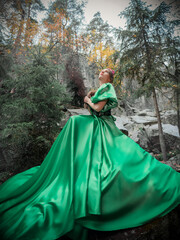 A beautiful woman in a long green dress with a corset and a decorative crown of branches and flowers on her head. Forest nymph on the background of rocks. Full length portrait.
