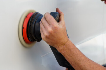 Close-up detail of the professional mechanic's hand, using the polishing machine on the left door of a white car, removing scratches and flaws and leaving it shiny, in his workshop in Granada.