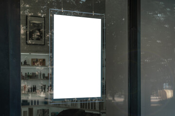 Commercial blank white signboard hanging vertically behind window glass of boutique or fashion store