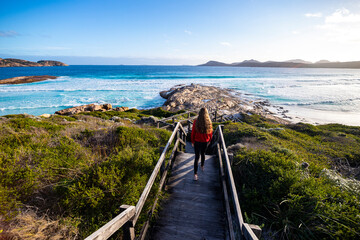 beautiful long-haired girl walks down stairs to paradise beach, sunset on lucky bay beach in west...