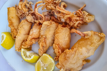 A plate full of fried squid with fresh lemon served in a local restaurant in coastal village of Vourvourou, Sithonia, Chalkidiki (Halkidiki), Greece, Europe Local traditional food. Sea fruit food