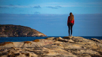 beautiful long-haired girl stands on the rocks above the ocean admiring the sunset; sunset on lucky...