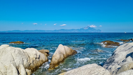 Naklejka premium Beautiful panoramic view of holy Mount Athos seen from Karydi beach, peninsula Sithonia, Chalkidiki (Halkidiki), Greece, Europe. Summer vacation at Aegean Mediterranean Sea. Rock formations in the bay