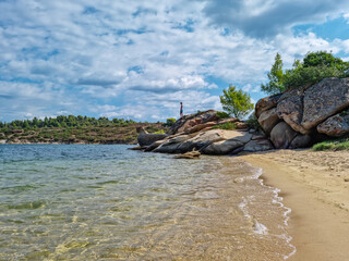 Man in swimsuit staning on rocks with panoramic view of holy Mount Athos from Fava sand beach,...